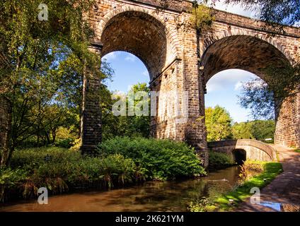 Un viadotto ferroviario storico che torreggia su una serratura sul canale stretto di Huddersfield, a Uppermill, Oldham, Greater Manchester, UK Foto Stock