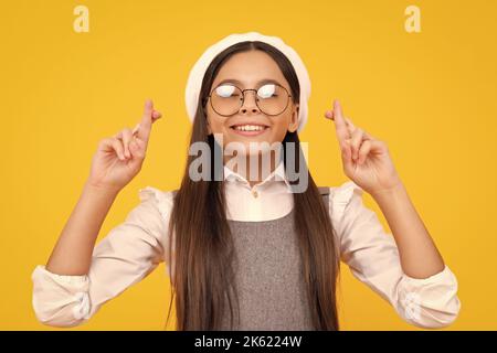 Ragazza adolescente che le incrocia le dita e che desidera buona fortuna, isolato su sfondo giallo studio con spazio copia. Foto Stock