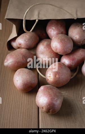 Patate rosse nuove crude in sacchetto di carta su fondo di legno Foto Stock