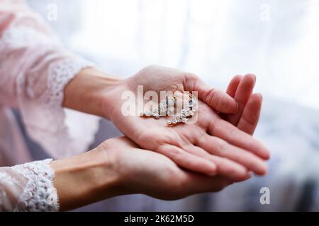 la ragazza in un bel vestito bianco tiene gli orecchini nelle sue mani Foto Stock