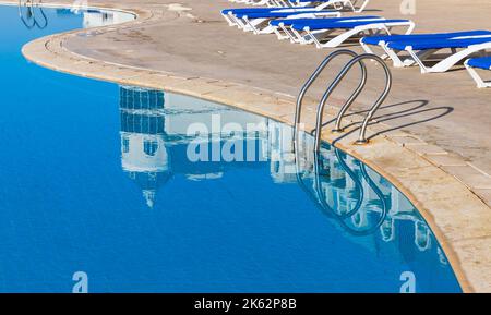 Una piscina esterna vuota con ringhiere metalliche e lettini Foto Stock