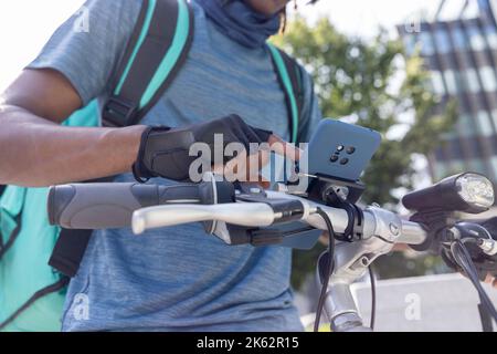 Primo piano di Courier on Bike consegna di cibo da asporto in città controllo delle direzioni e dettagli dell'ordine sul telefono cellulare Foto Stock