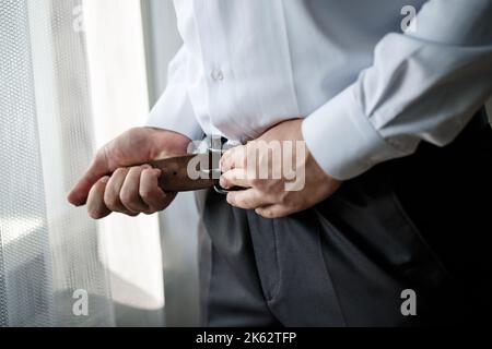 Uomo d'affari elegante allacciando una cintura sui pantaloni lui indossa una camicia bianca Foto Stock