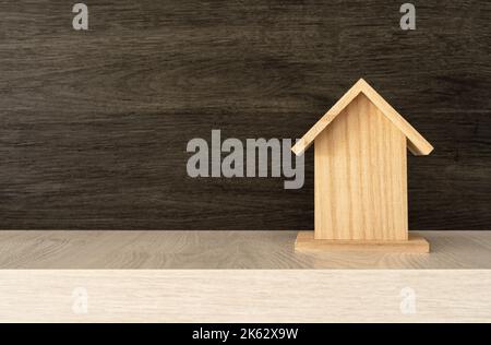 Concetto di proprietà. Piccola casa di legno 3D su sfondo di legno nero con spazio sulla sua sinistra. Foto Stock