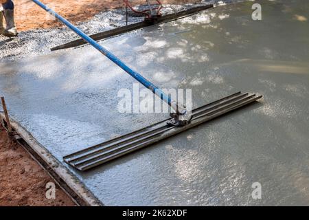 Intonacando cemento pavimento di patio in cemento con utilizzando cazzuola lunga è stato fatto da muratore lavorando su di esso. Foto Stock