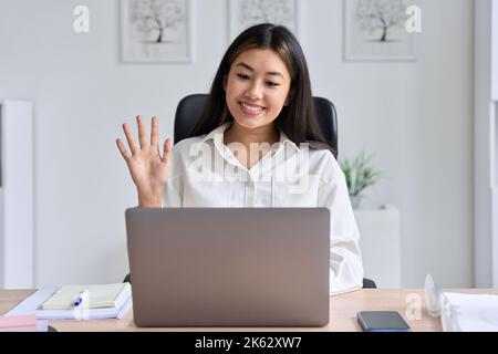 Donna asiatica d'affari che si sta muovendo le mani per salutare il partner durante la videoconferenza Foto Stock