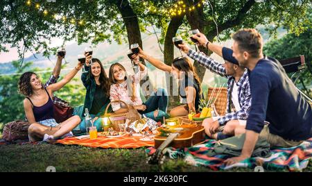 Amici felici che si divertono a vigneto al tramonto - giovani millenial brinda a picnic all'aria aperta sotto la luce string - concetto di amicizia giovanile con Foto Stock