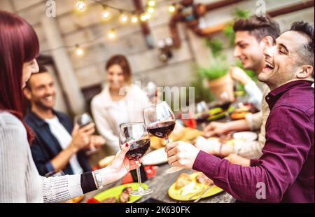 Amici felici che si divertono a bere vino rosso sul balcone durante la cena privata - giovani che mangiano insieme cibo barbecue al ristorante di moda - Dining l Foto Stock