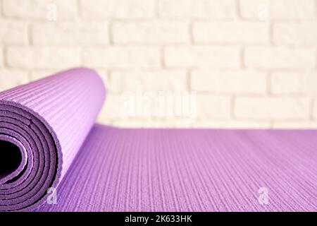 Sottile tappeto viola yoga sul pavimento in legno nella moderna palestra. Accessori per allenamento e aerobica Foto Stock