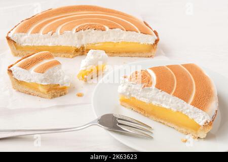 Tagliare la crostata di limone con la meringa sulla carta da forno accanto a una porzione di crostata di limone sulla piastra con una forchetta. Foto Stock