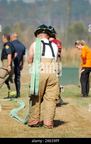 Pompieri che combattono un incendio a spazzola nella zona di Atlanta con acqua e attrezzature di sicurezza e tubo spiralato della sua spalla indossando sospensori Foto Stock