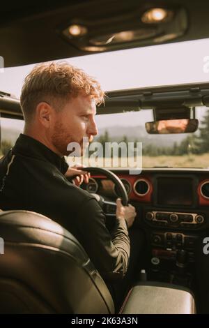 Giovane uomo bello capelli rossi guida veicolo terreno su un viaggio in natura Foto Stock
