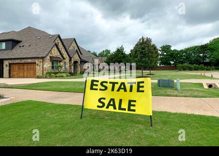 Foto all'aperto di casa residenziale con strada e prato pulito di fronte ad esso, grande segno giallo con iscrizione di vendita proprietà. Vendita di ville. Foto Stock