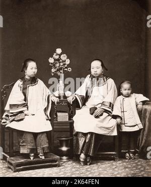 Fotografia d'annata del XIX secolo: Donne cinesi con piedi rilegati, fotografate in uno studio con un bambino piccolo. Cina. circa 1880's. Foto Stock