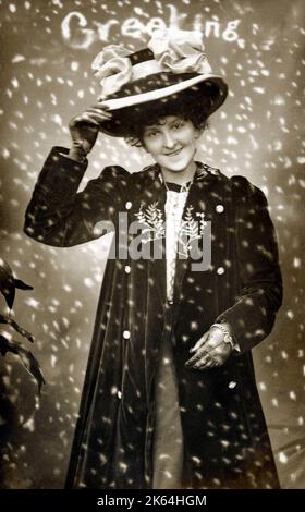 Una giovane donna con un grande cappello a fiocco e un elegante cappotto di velluto sorride un saluto attraverso la neve invernale che cade. Foto Stock