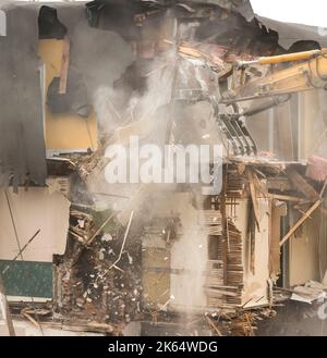 Demolizione di un edificio con un grande retroescavatore. Giornata di Overcast. Molta polvere nell'aria. Molti detriti che cadono. Foto Stock