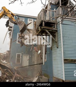 Demolizione di un edificio con un grande retroescavatore. Giornata di Overcast. L'aria è polverosa e sono presenti detriti dalla demolizione. Foto Stock