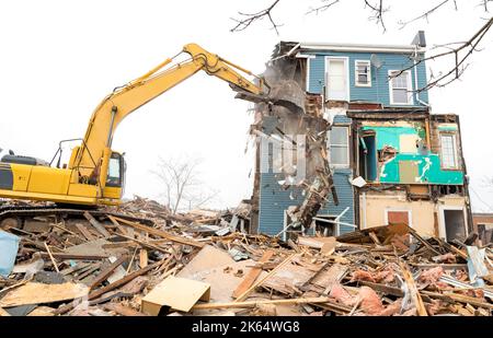Demolizione di un edificio con un grande retroescavatore. Giornata di Overcast. L'aria è polverosa. Il retroescavatore si trova sui detriti della demolizione. I detriti cadono da una parete. Foto Stock