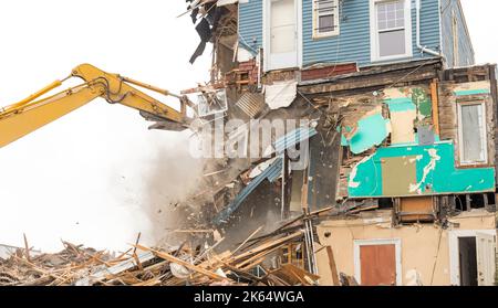 Demolizione di un edificio con un grande retroescavatore. Giornata di Overcast. L'aria è polverosa. Molti detriti dalla demolizione. Molti detriti cadono da un muro. Foto Stock