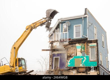 Demolizione di un edificio con un grande retroescavatore. Giornata di Overcast. L'aria è polverosa. Retroescavatore sembra che stia per prendere un boccone fuori dall'edificio. Foto Stock