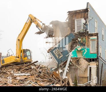 Demolizione di un edificio con un grande retroescavatore. Giornata di Overcast. L'aria è polverosa. Il retroescavatore si trova sui detriti della demolizione. Molti detriti. Foto Stock