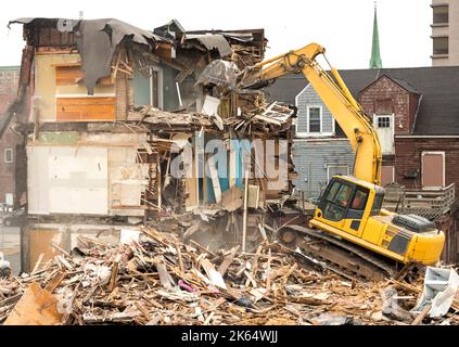 Demolizione di un edificio con un grande retroescavatore. Giornata di Overcast. L'aria è polverosa e sono presenti detriti dalla demolizione. Il retroescavatore si trova su una montagna di detriti. Foto Stock