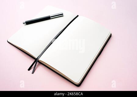 Aprire il giornale puntato o il notebook con pagine vuote e una penna su sfondo rosa pastello Foto Stock