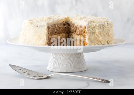 Una torta di carote ricoperta di cocco fatta in casa con una fetta grande prelevata dal centro. Foto Stock