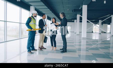 Il gruppo multietnico di uomini e donne d'affari parla e studia il progetto all'interno di un moderno edificio commerciale. Concetto di business e comunicazione. Foto Stock