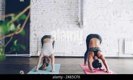 La giovane ragazza bionda sta godendo la pratica individuale di yoga con un'istruttrice femminile amichevole in studio luce. Le donne stanno facendo la sequenza di asana sui tappetini luminosi. Atmosfera accogliente e rilassante. Foto Stock