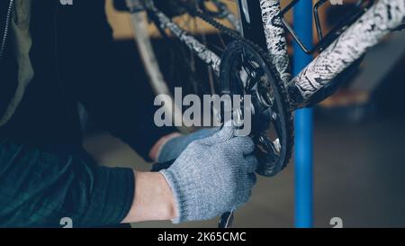 Foto ravvicinata di mani forti maschili in guanti protettivi che riparano il battistrada rotto della bicicletta con una chiave in officina. Professione, persone e concetto di manutenzione. Foto Stock