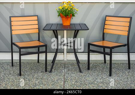 Tavolo all'aperto e due sedie vicino alla parete presso la caffetteria. Fiori sul tavolo e sedie all'aperto sulla strada. Nessuno, foto di strada, focus selettivo Foto Stock