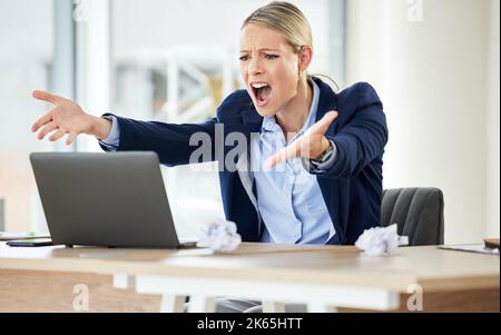 Una giovane donna d'affari caucasica che urla mentre usa un computer portatile in un ufficio al lavoro. Donna che ha una giornata stressante al lavoro e mostrando la sua frustrazione Foto Stock