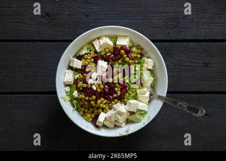 insalata di verdure con cavolo iceberg piselli e formaggio feta e fagioli su un piatto su un tavolo di legno, insalata di verdure, senza carne, verdure Foto Stock