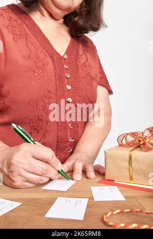 Donna matura irriconoscibile che scrive, facendo le schede fatte a mano per mettere sui suoi regali di Natale. Design semplice con spazio di copia. Foto Stock