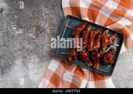 Ali di pollo Hoisin su spiedini di legno su un piatto rettangolare su sfondo scuro. Vista dall'alto, disposizione piatta Foto Stock
