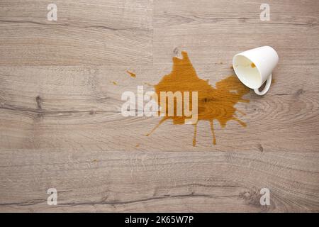 Una tazza di caffè è caduta su laminato, caffè versato sul pavimento. Concentratevi sulla pozza. Giacitura piatta. Vista dall'alto. Foto Stock