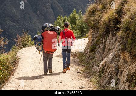 Sherpa che trasporta le borse pesanti di un turista in Nepal sulla via dell'Everest durante il viaggio verso la stazione di base del monte Everest Foto Stock