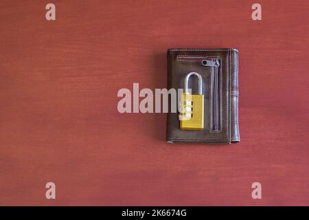 Un portafoglio isolato in pelle vecchia con un lucchetto numerico chiuso in oro sulla parte superiore su uno sfondo colorato e ruvido studio. Economia domestica e finanza conce Foto Stock