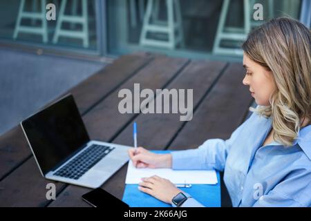 Ritratto di una donna d'affari che prende appunti, studia sul suo computer, seduto fuori nel parco. Giovane donna che scrive, videoconferenza sul notebook Foto Stock