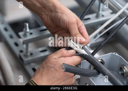Le mani dell'elettricista rimuovono l'isolamento elettrico del cavo per il collegamento ai terminali. Il tecnico elettrico esegue lavori elettrici in una scatola di derivazione Foto Stock