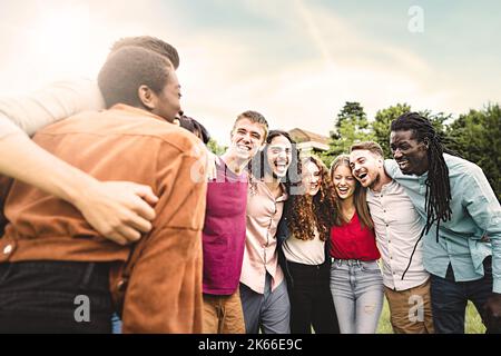 Gruppo multietnico di giovani diversi che si divertono a abbracciarsi insieme camminando ridendo e interagendo insieme braccio su spalle nel parco - unità, Foto Stock