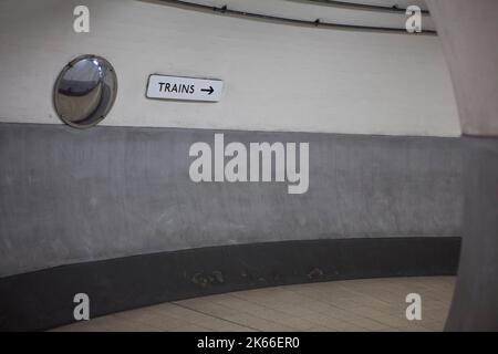 Un cartello con la scritta 'TRAINS' (TRENI) con una freccia che punta a destra, giù per un tunnel della metropolitana alla stazione di Holland Park sulla Central Line nella parte ovest di Londra Foto Stock