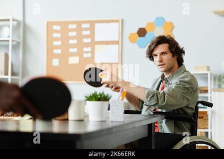 Ritratto di giovane caucasico con disabilità giocando a ping pong in ufficio sala pausa, spazio copia Foto Stock