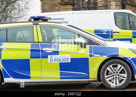 Vista laterale bassa dei veicoli della polizia parcheggiati senza agenti all'interno. Un'indagine forense firmata furgone è sullo sfondo. Foto Stock