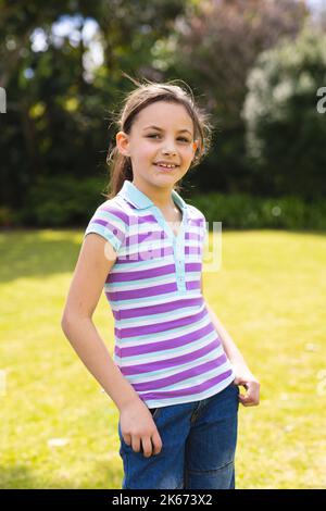 Ritratto verticale di una giovane caucasica che indossa una t-shirt a righe e che si erge in giardino Foto Stock
