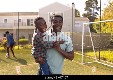 Buon padre e figlio afroamericano che trascorrono del tempo insieme e giocano a calcio all'aperto Foto Stock
