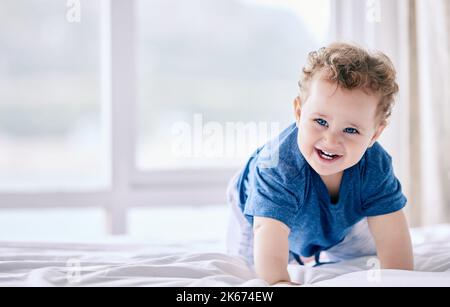 La mamma mi ha detto di rimanere, ma ho altri piani: Un adorabile ragazzino che strisciò sul letto di casa. Foto Stock