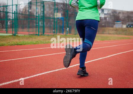 Atleta sportivo donna che corre sul campo sportivo in autunno. Primo piano delle sneakers e delle gambe femminili in pista. Stile di vita sano e attivo Foto Stock