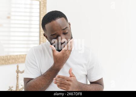 Ritratto di giovane afroamericano che applica crema nutriente del viso o balsamo in vasca da bagno, concetto di cura della pelle. Foto Stock